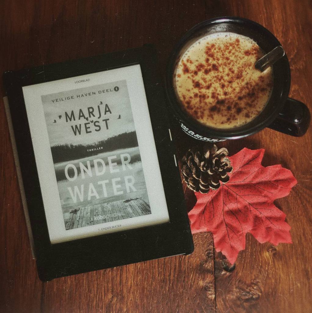 Ebook Onder water van Marja West op Kobo e-reader met een cappuccino en herfst decoraties ernaast op een houten achtergrond.